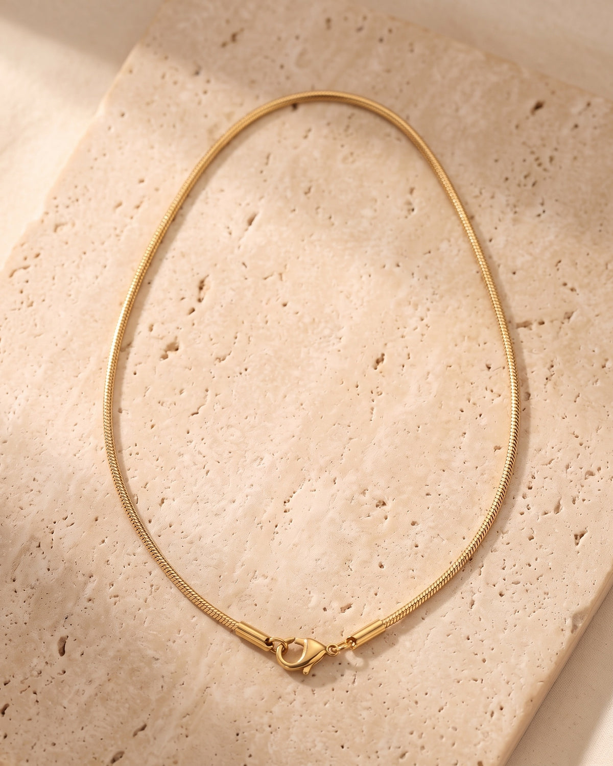 Entire Atlas 0.9 mm snake chain in gold-tone steel, lying flat on warm stone