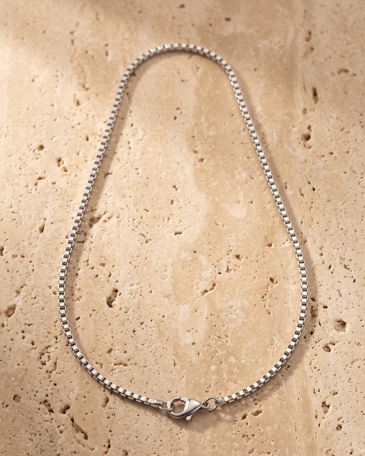 The whole silver-tone Atlas 1.5 mm box chain laid on warm stone