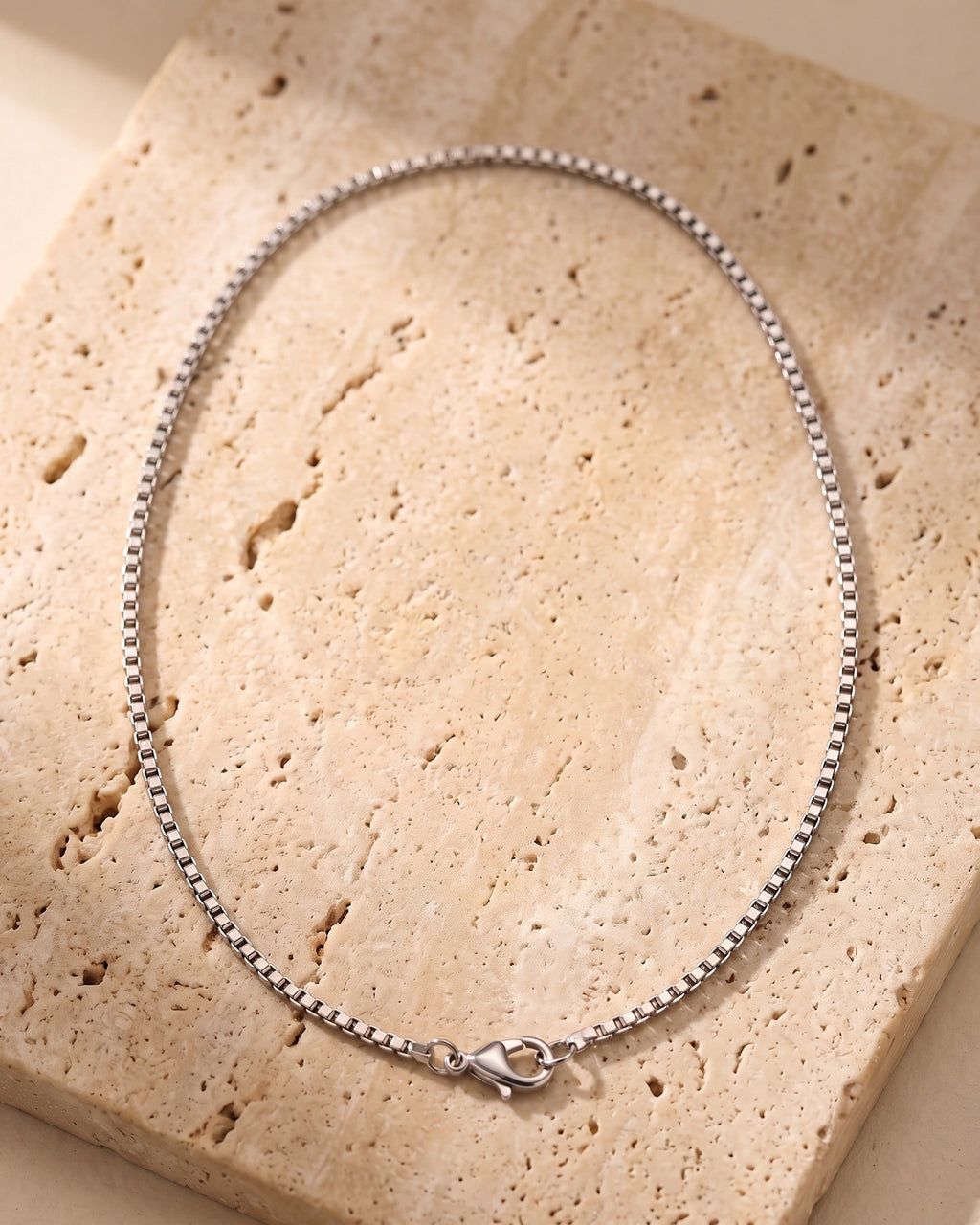The whole silver-tone Atlas 1.5mm Box Chain lying on warm travertine stone