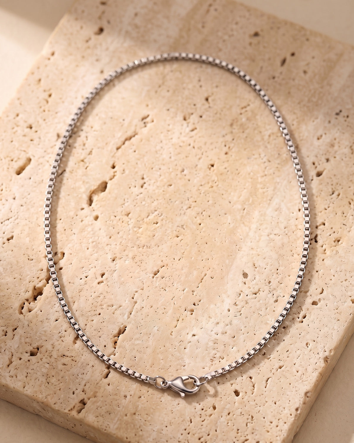 The whole silver-tone Atlas 1.5mm Box Chain lying on warm travertine stone