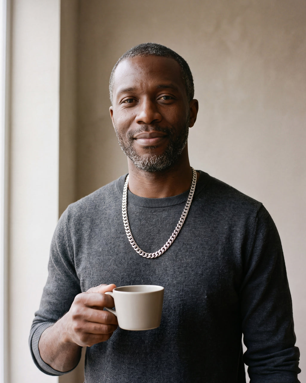 Smiling man in a charcoal knit holding a coffee cup wearing the silver Atlas 10 mm Cuban link chain