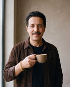 Man in a brown suede overshirt holding a coffee cup, wearing the gold-tone Atlas Cuban bracelet