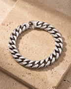 Entire Atlas 10 mm Cuban link bracelet in silver-tone steel, lying flat on warm stone