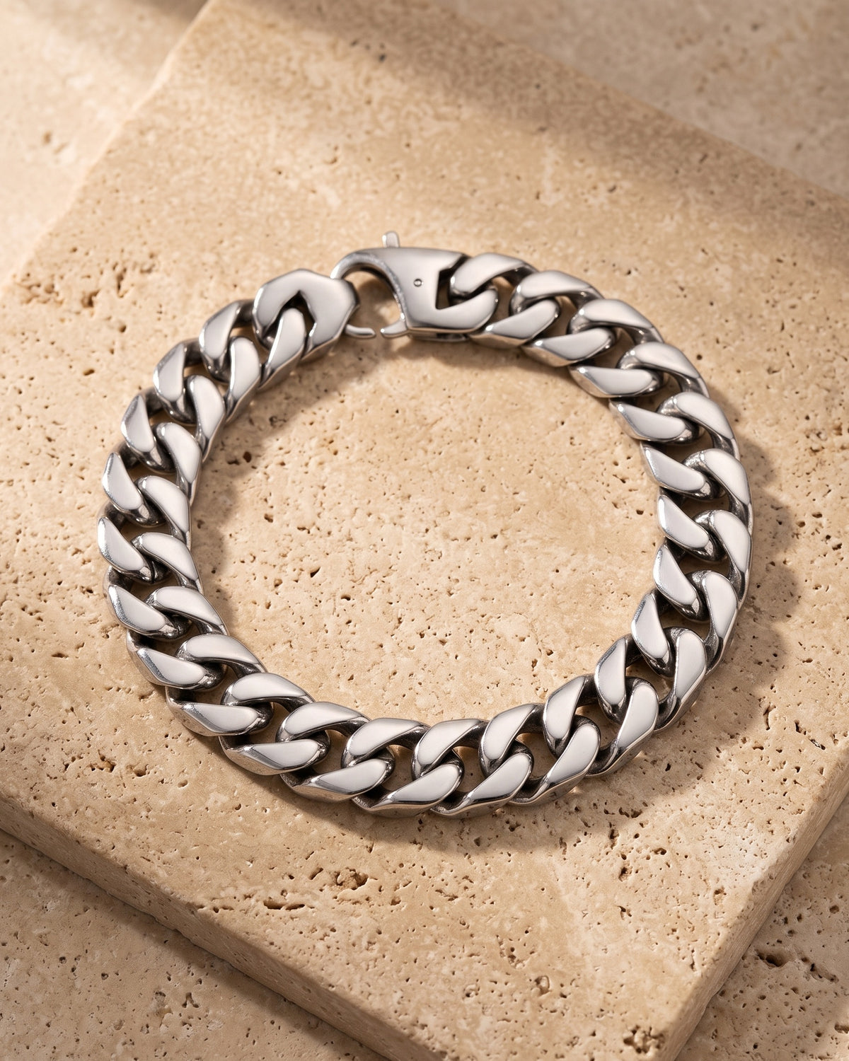 Entire Atlas 10 mm Cuban link bracelet in silver-tone steel, lying flat on warm stone