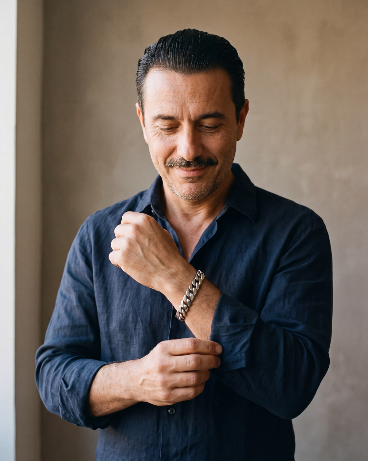 Man in a navy linen shirt by a window wearing the Atlas 10 mm Cuban link bracelet in silver-tone steel