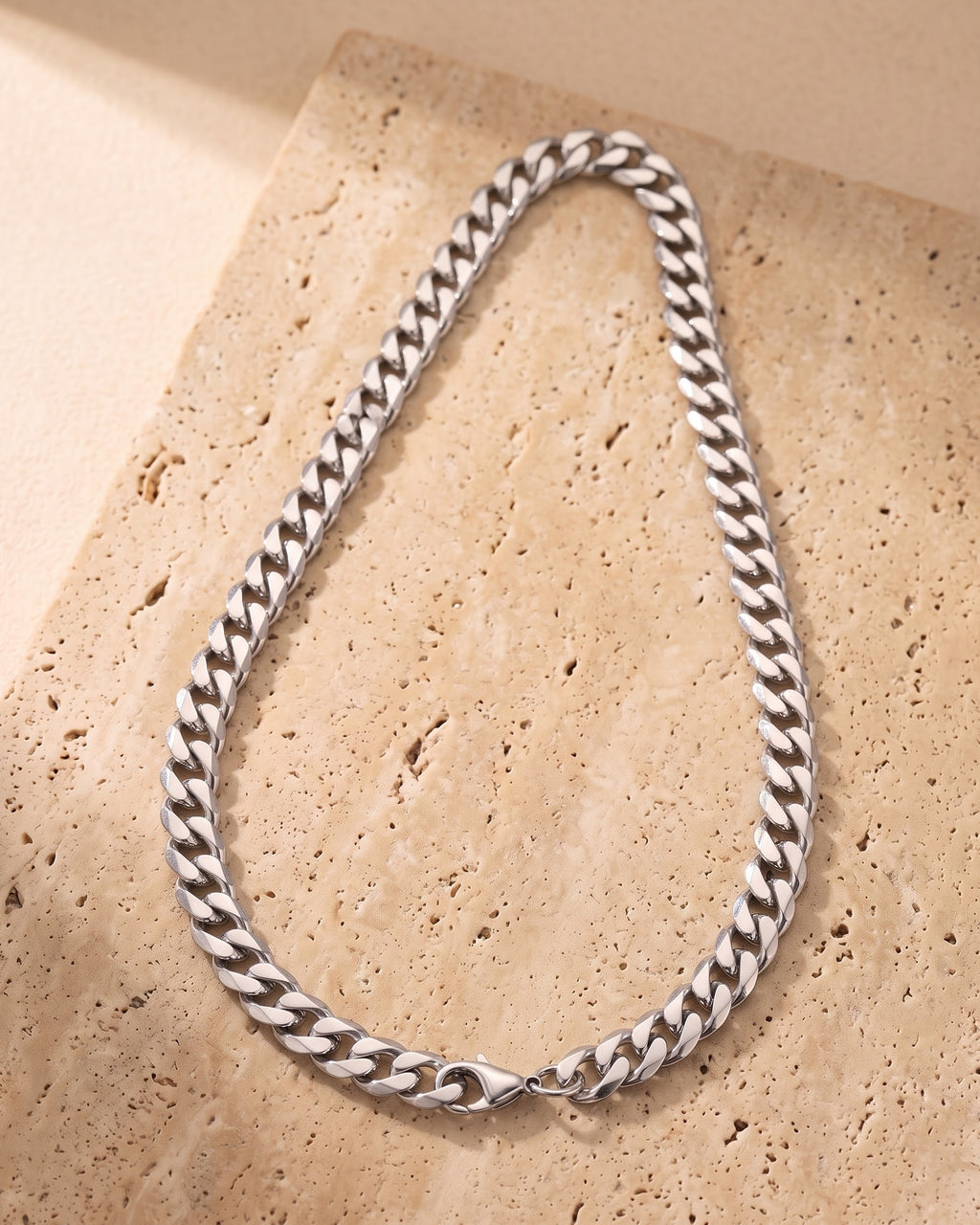 The whole silver-tone Atlas 10 mm Cuban link chain laid on warm stone