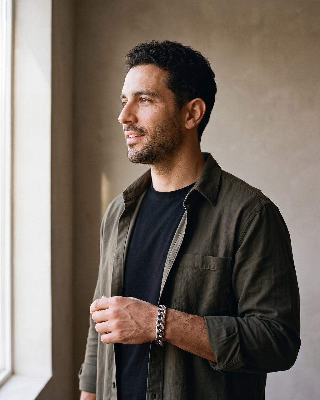 Man in a dark olive overshirt open over a black t-shirt by a window wearing the silver Atlas 11mm Cuban Link Bracelet