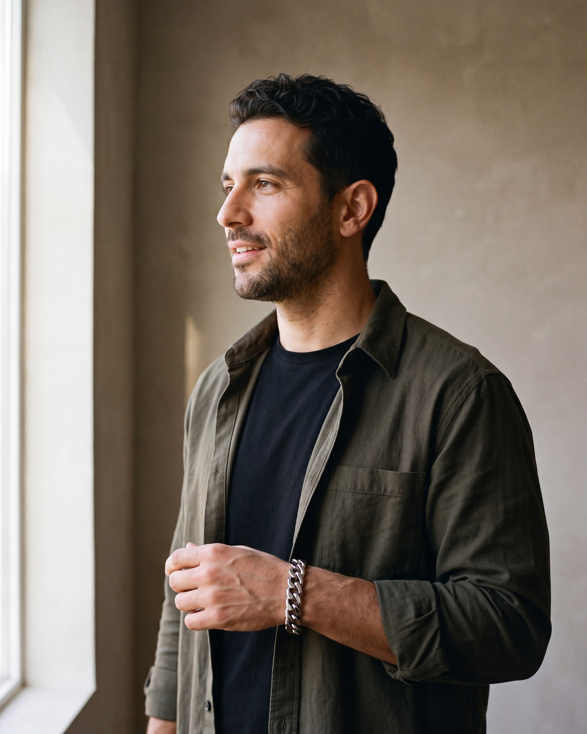 Man in a dark olive overshirt open over a black t-shirt by a window wearing the silver Atlas 11mm Cuban Link Bracelet
