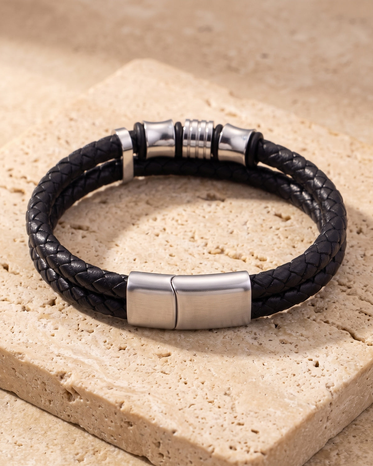 The whole silver-tone Atlas 14mm Braided Leather Bracelet with Magnetic Clasp lying on warm travertine stone
