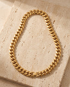 The whole Atlas 14 mm Cuban chain in gold-tone stainless steel laid on warm stone