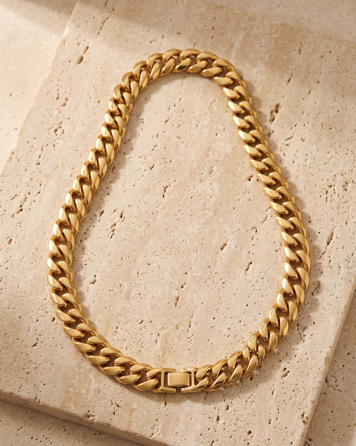 The whole Atlas 14 mm Cuban chain in gold-tone stainless steel laid on warm stone