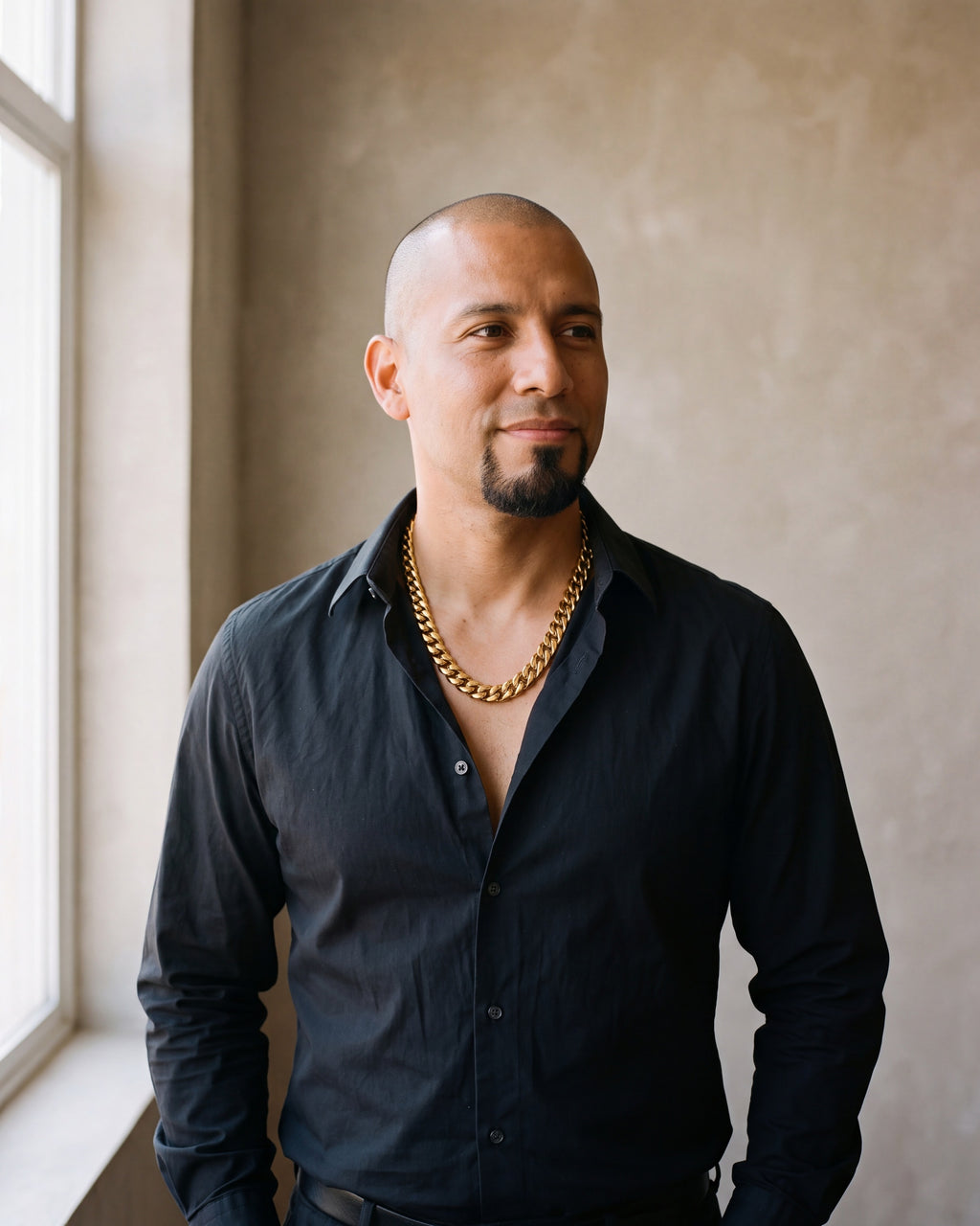 Man in a black shirt by a window wearing the Atlas 14 mm Cuban chain in gold-tone steel