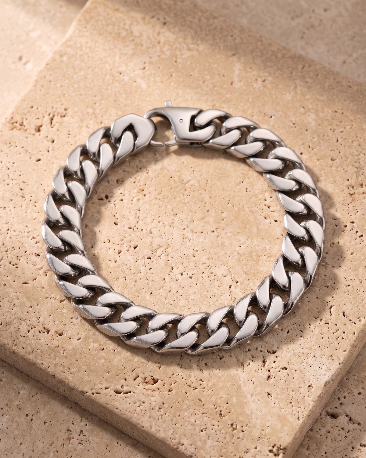 The silver Atlas 15mm Titanium Steel Cuban Bracelet laid on warm travertine stone