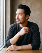 Man in a charcoal sweater seated at a wooden table wearing the black Atlas 2 mm polished band