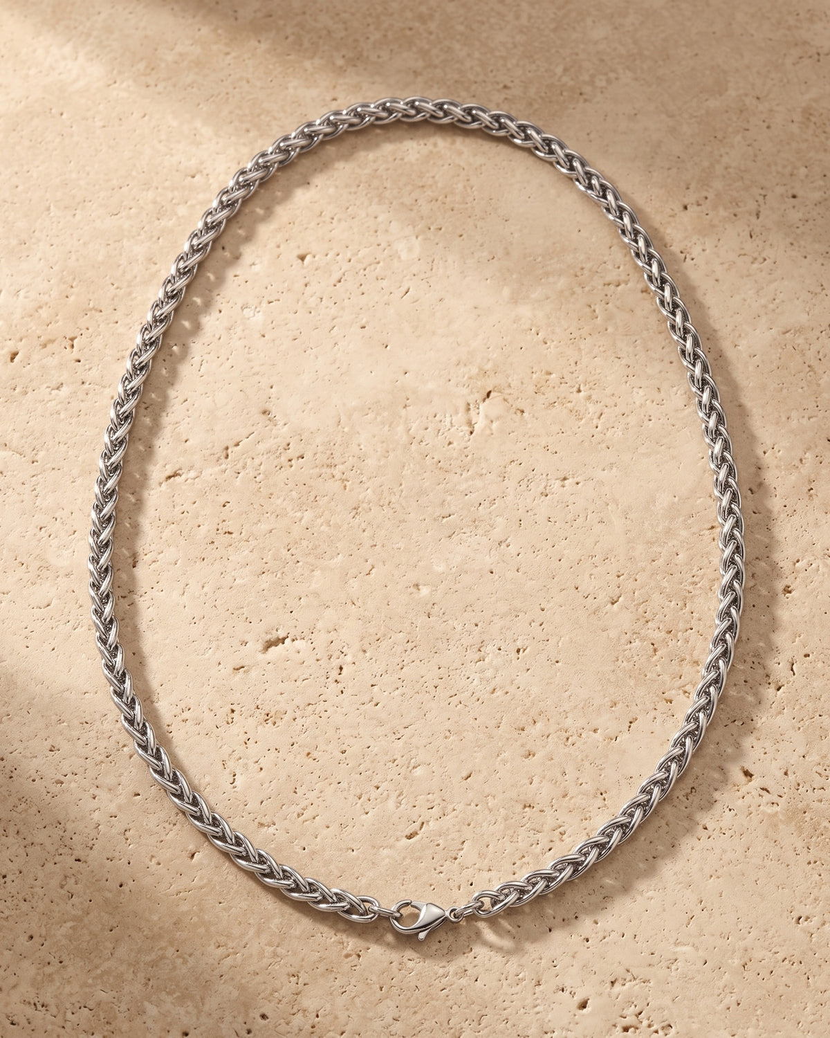 The whole silver-tone Atlas wheat chain lying on warm travertine stone