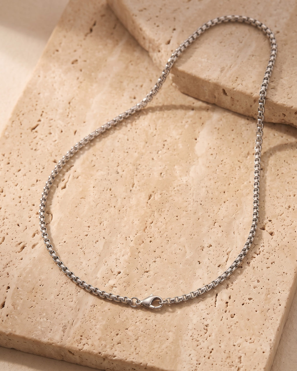 The silver Atlas 2mm Rolo Link Chain in Stainless Steel laid on warm travertine stone