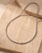 The silver Atlas 2mm Rolo Link Chain in Stainless Steel laid on warm travertine stone