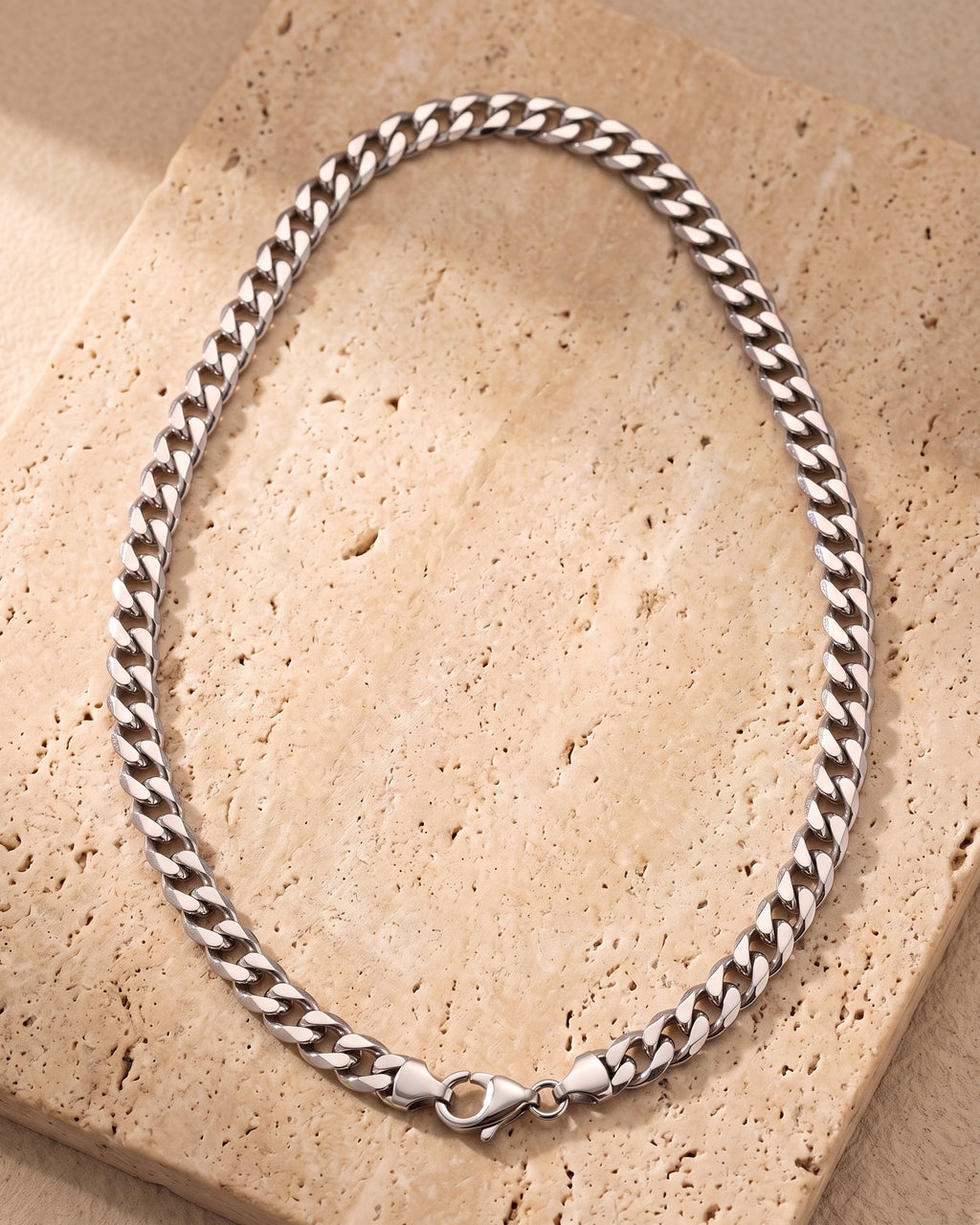 Entire Atlas curb chain in silver-tone steel, lying flat on warm stone