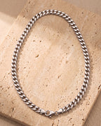 Entire Atlas curb chain in silver-tone steel, lying flat on warm stone