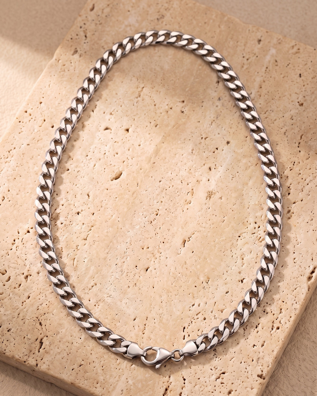 Entire Atlas curb chain in silver-tone steel, lying flat on warm stone