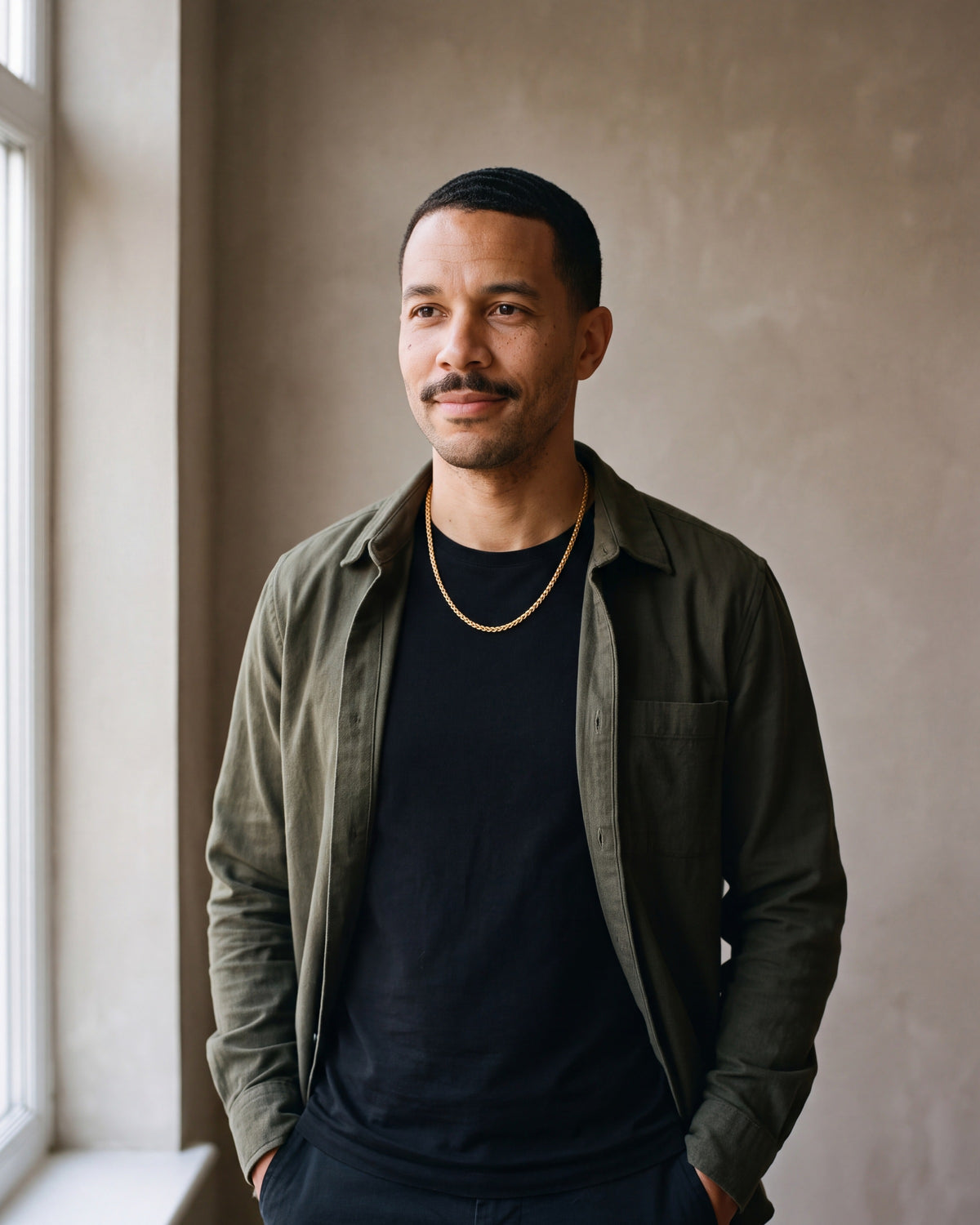 Man in an olive overshirt with his hands in his pockets wearing the gold-tone Atlas 3 mm wheat chain