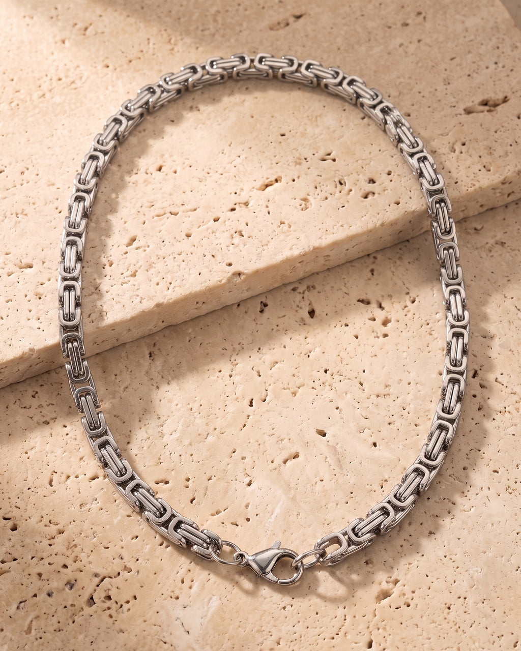 Silver-tone Atlas Byzantine chain laid whole on warm stone