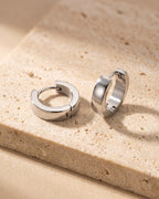 The whole silver-tone Atlas 4mm hoop earrings lying on warm travertine stone