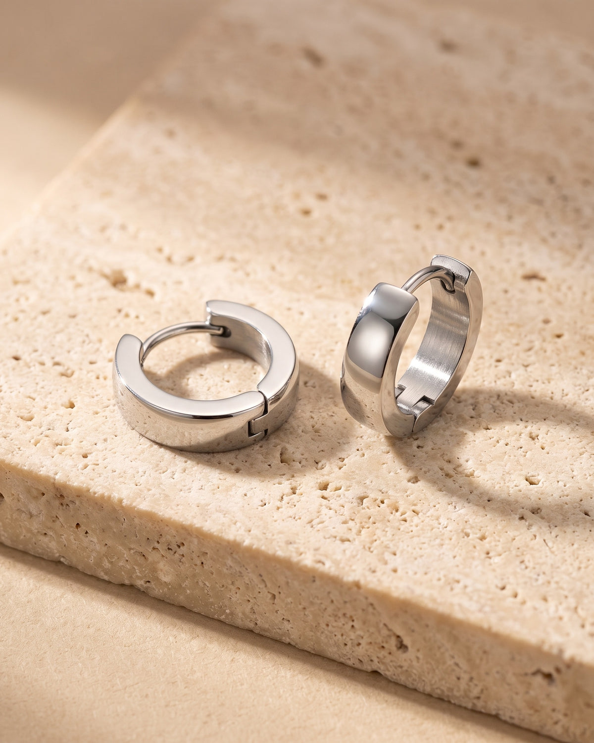 The whole silver-tone Atlas 4mm hoop earrings lying on warm travertine stone