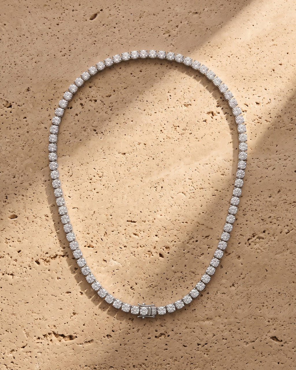 The silver Atlas 4mm Tennis Chain laid on warm travertine stone