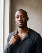 Man in a charcoal knit henley wearing the Atlas 4 mm wheat chain in gold-tone steel