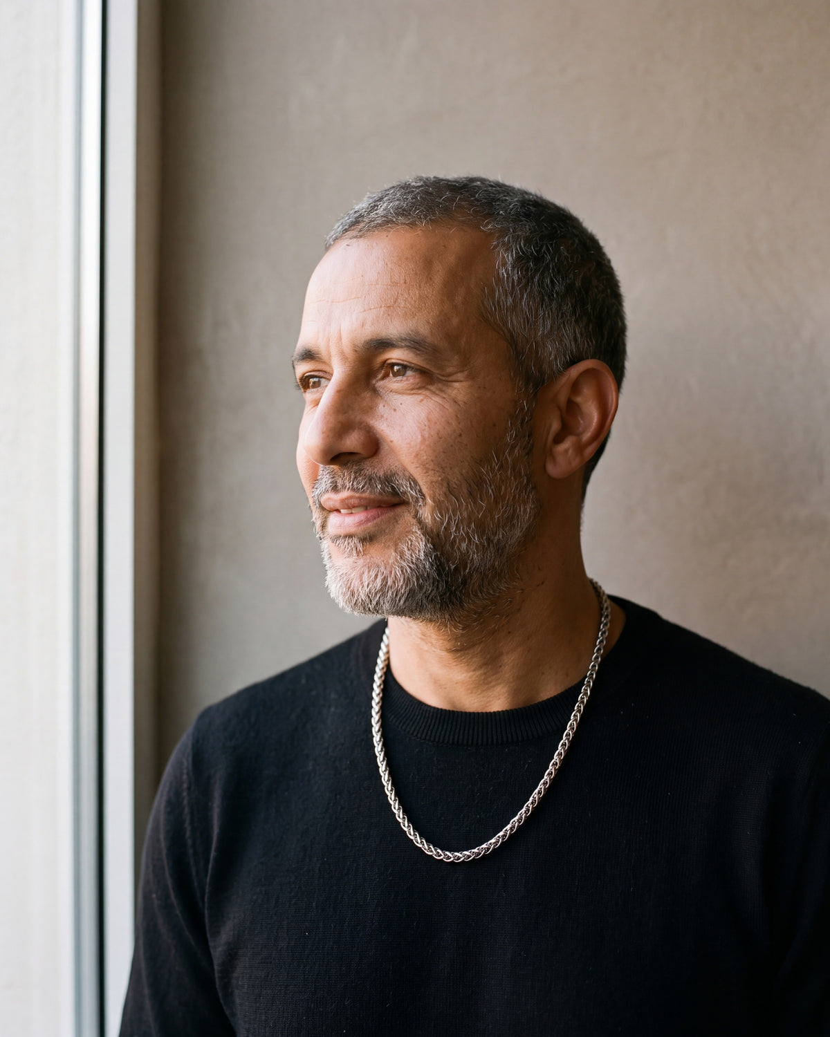 Man in a black merino sweater by a window wearing the Atlas 4 mm wheat chain in silver-tone steel