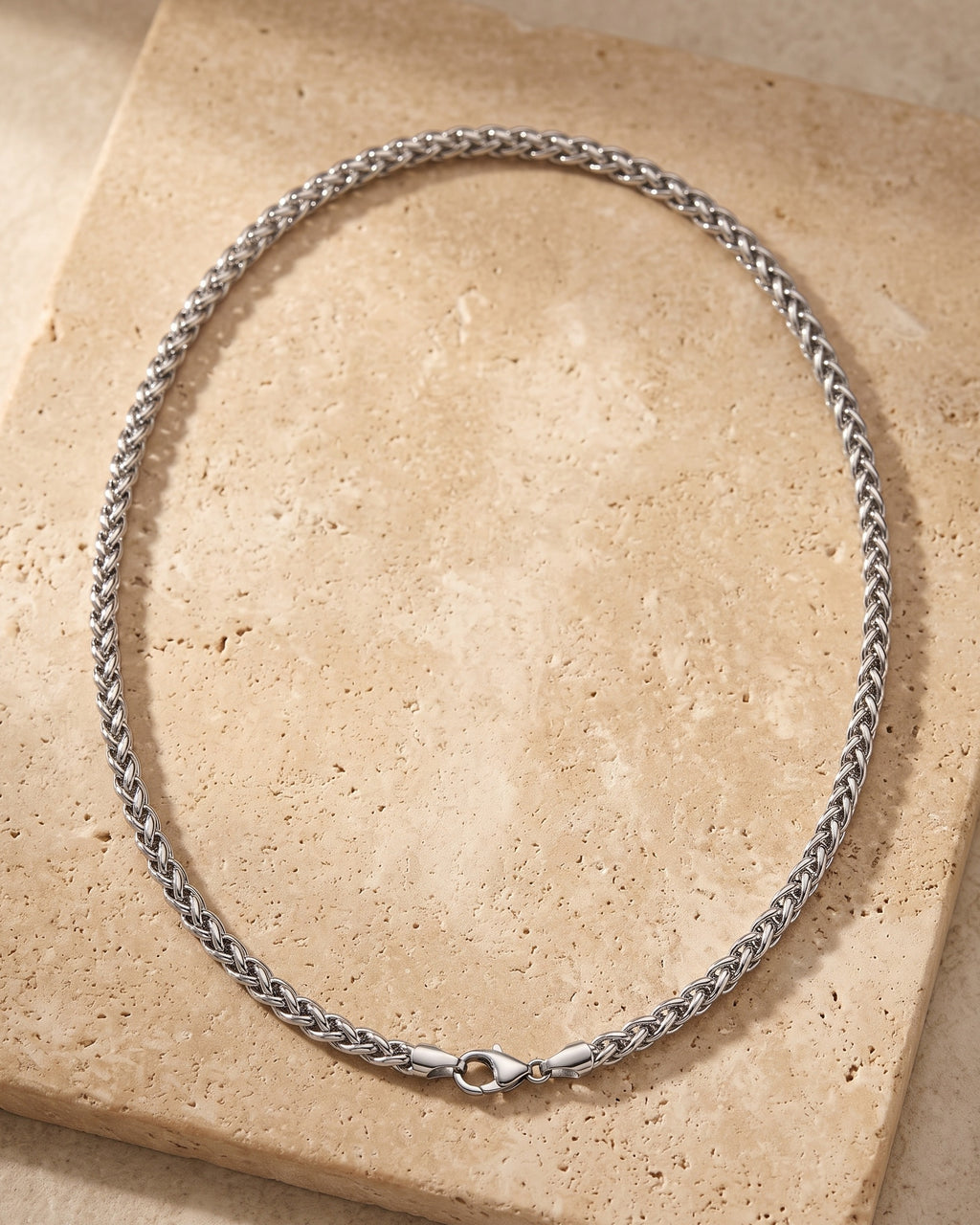 Entire Atlas 4 mm wheat chain in silver-tone steel, lying flat on warm stone