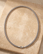 Entire Atlas 4 mm wheat chain in silver-tone steel, lying flat on warm stone