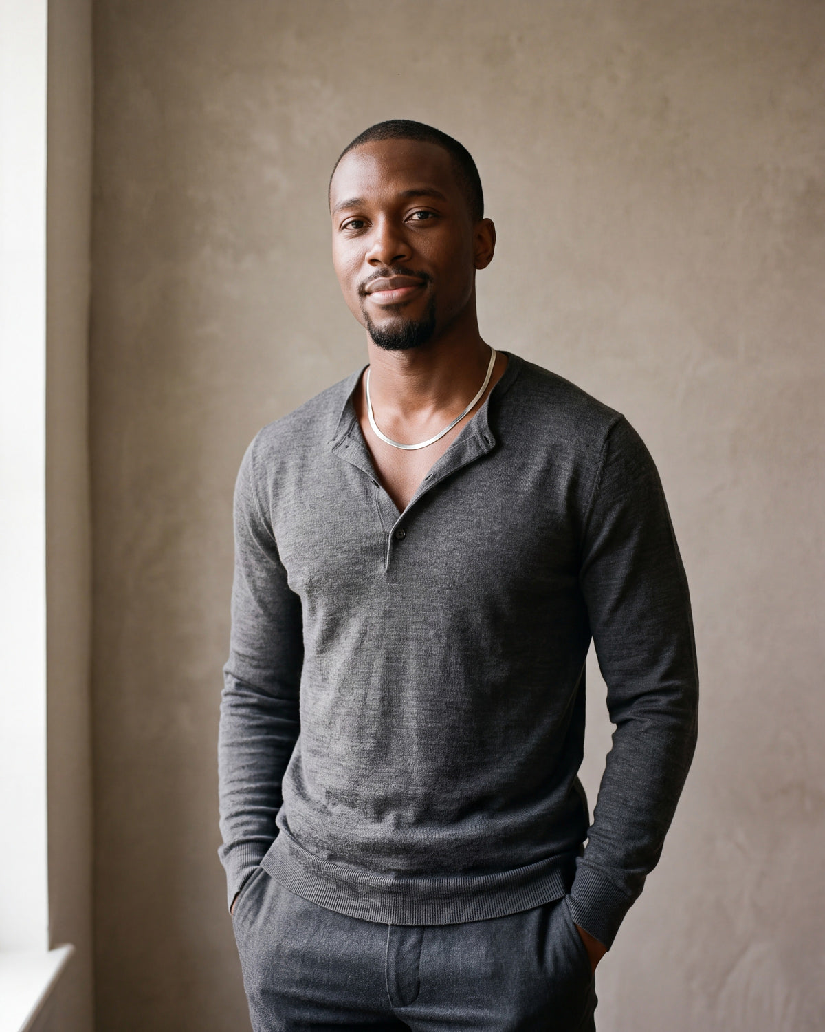 Man in a charcoal knit henley by a window wearing the Atlas 5 mm flat snake chain in silver-tone steel