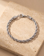 Entire Atlas 5 mm rope chain bracelet in silver-tone steel, lying flat on warm stone