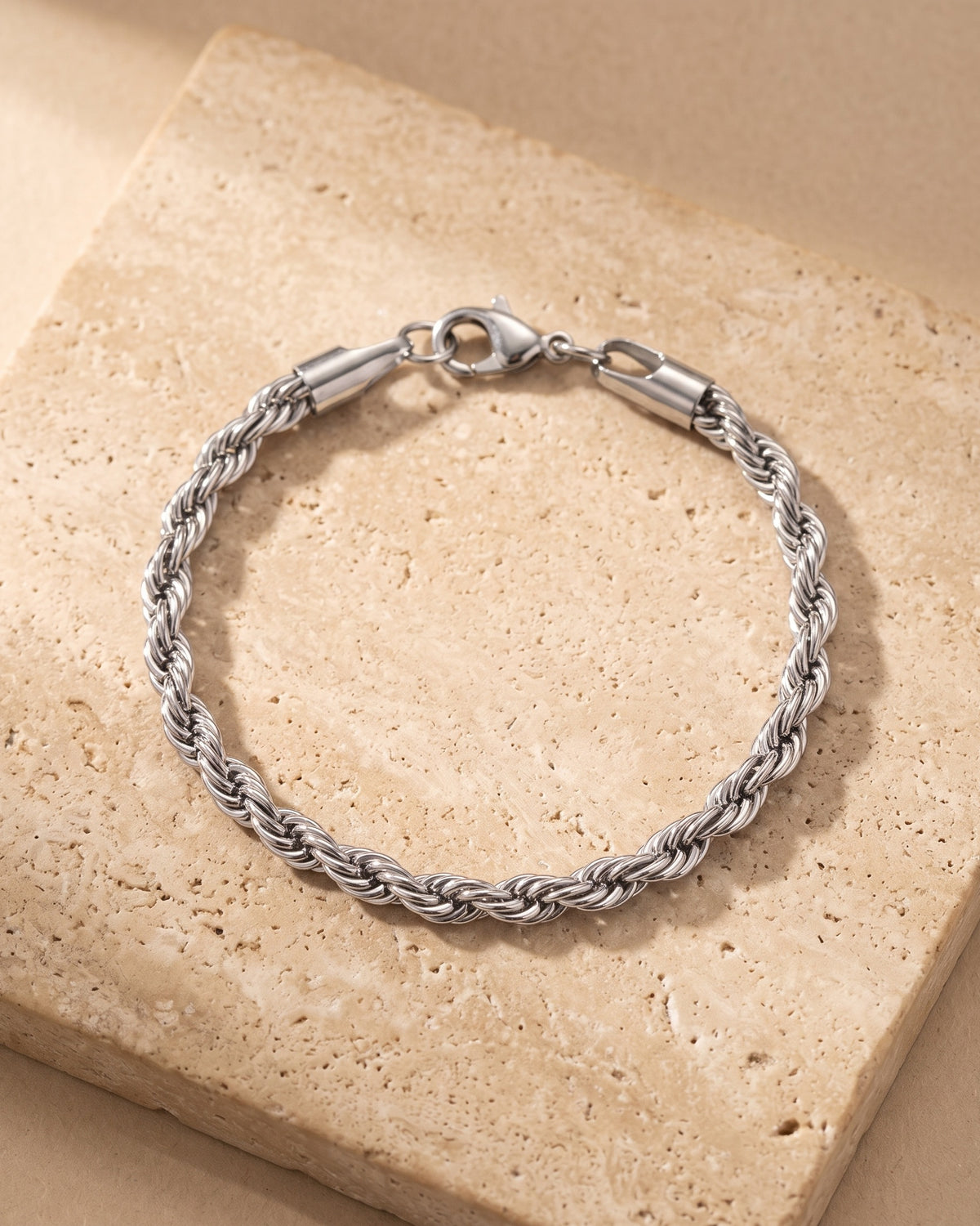 Entire Atlas 5 mm rope chain bracelet in silver-tone steel, lying flat on warm stone