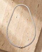 Entire Atlas 5 mm flat snake chain in silver-tone steel, lying flat on warm stone