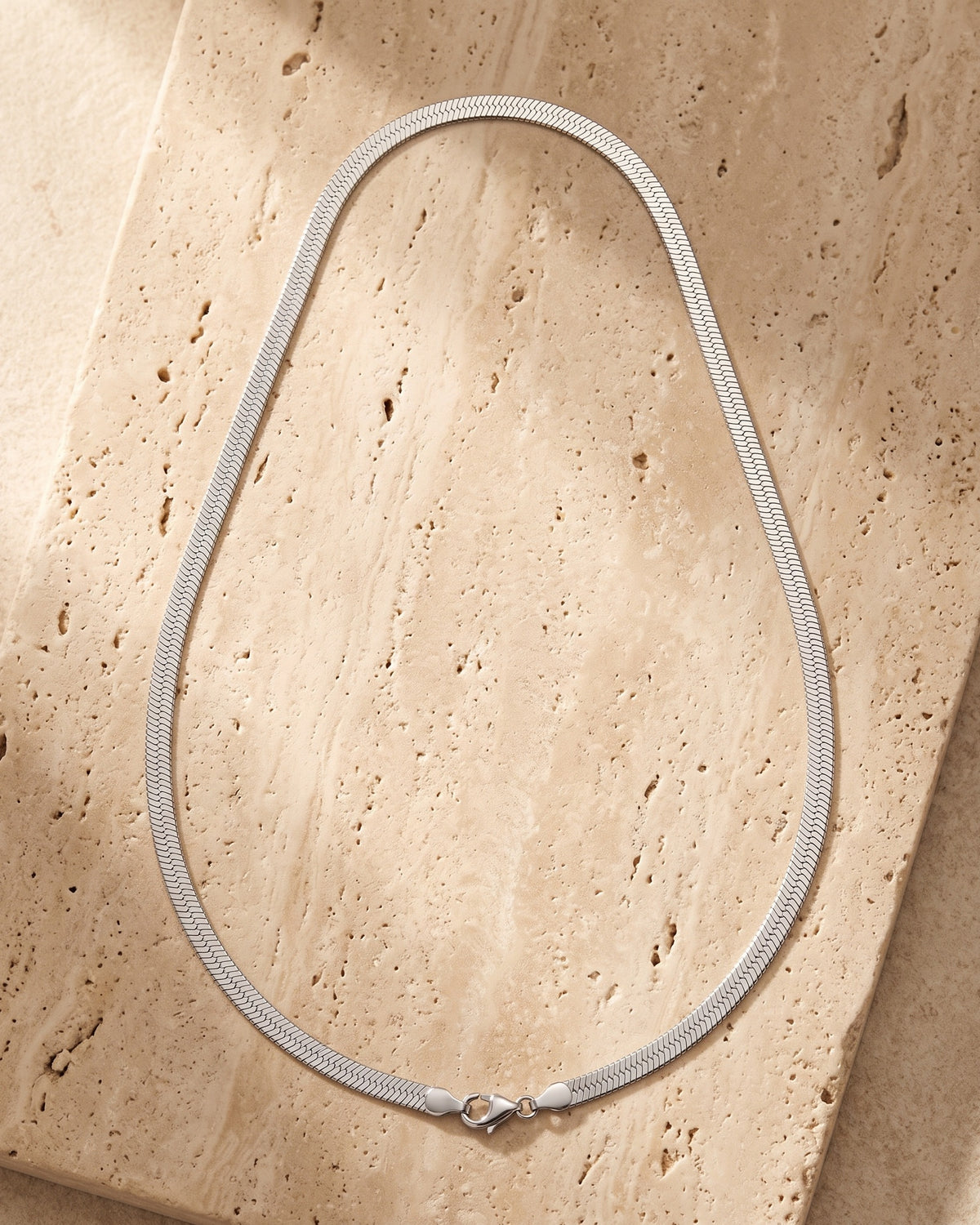 Entire Atlas 5 mm flat snake chain in silver-tone steel, lying flat on warm stone