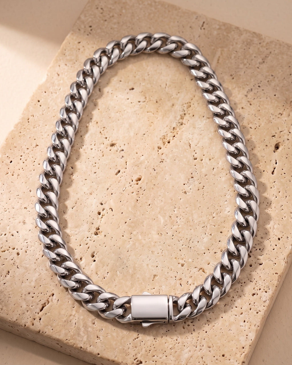 The whole silver-tone Atlas heavy Cuban chain laid on warm stone with its box clasp closed