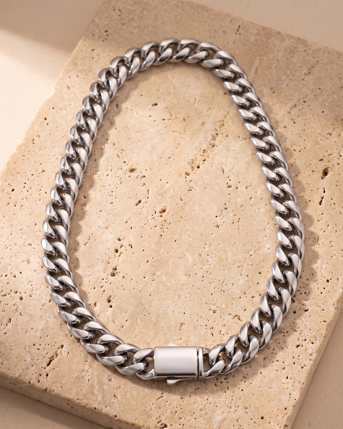 The whole silver-tone Atlas heavy Cuban chain laid on warm stone with its box clasp closed