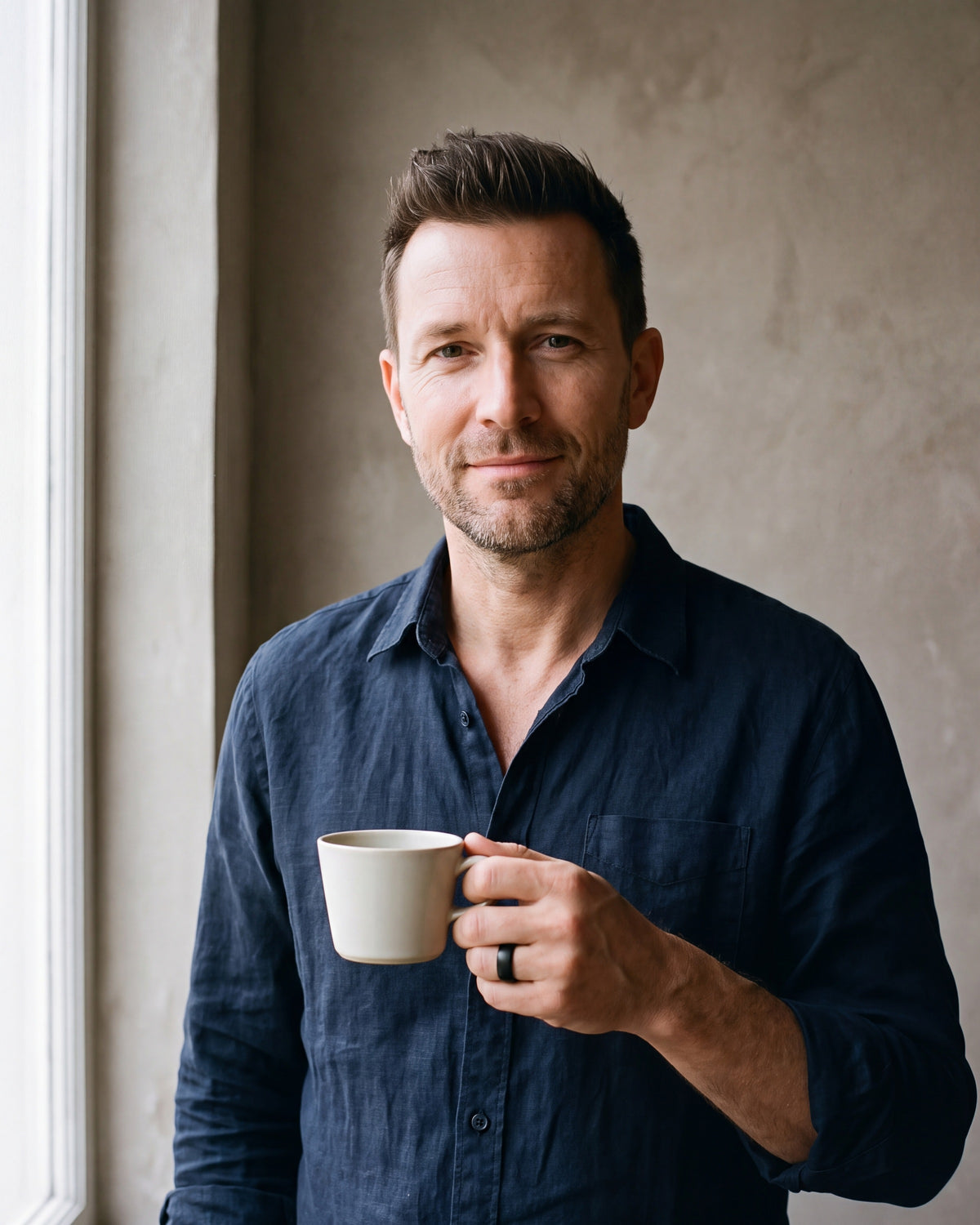 Man in a navy linen shirt holding a coffee cup wearing the black Atlas 8 mm brushed black tungsten carbide ring