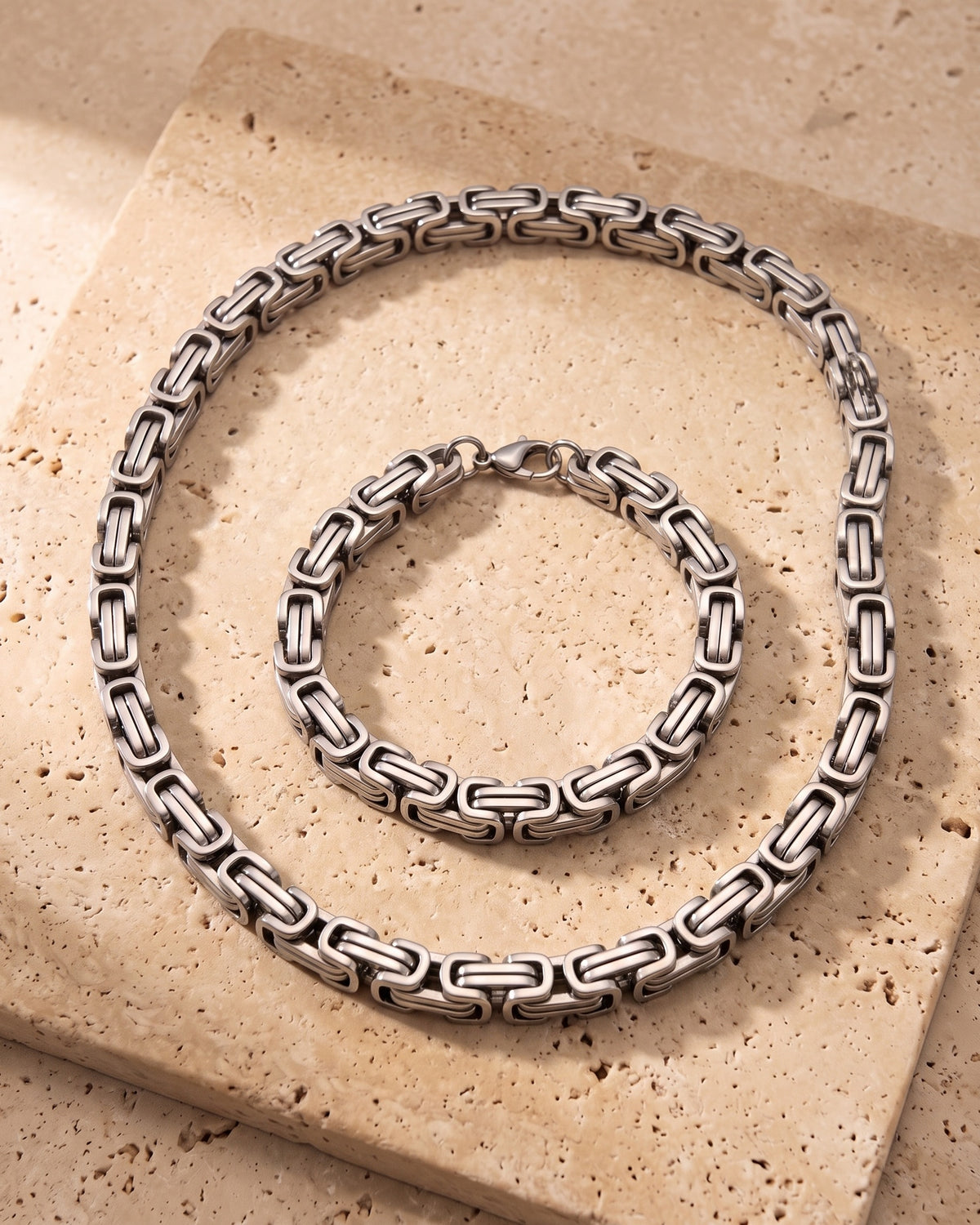 The whole silver-tone Atlas byzantine chain and bracelet set lying on warm travertine stone
