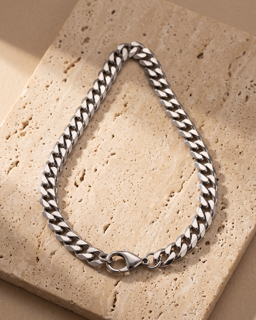 The whole silver Atlas 9 mm Cuban chain laid on warm stone, lobster clasp closed