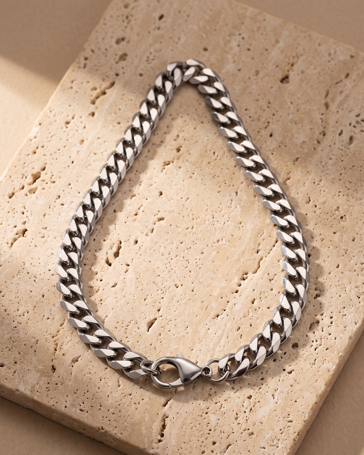 The whole silver Atlas 9 mm Cuban chain laid on warm stone, lobster clasp closed
