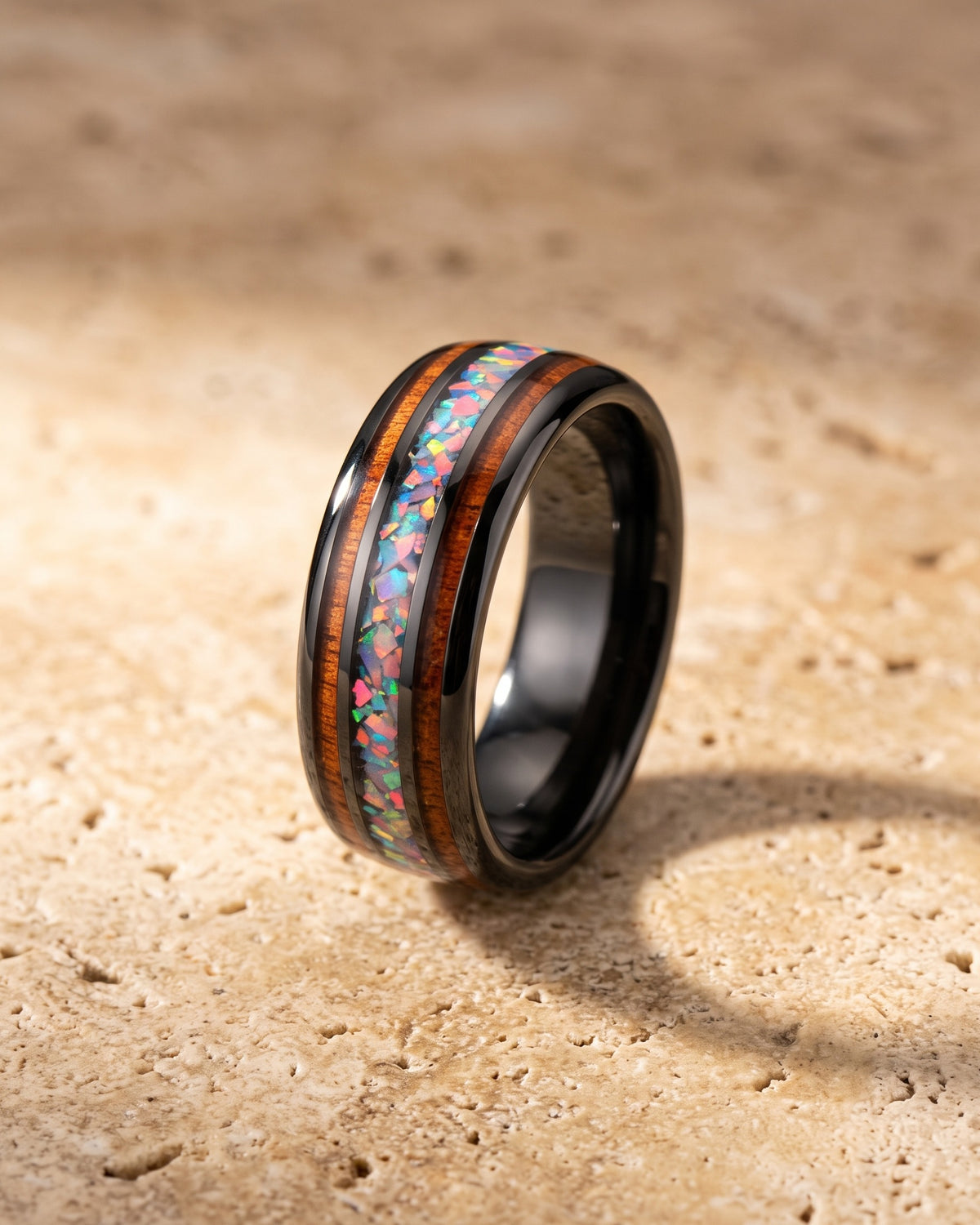 The Atlas acacia wood and opal black tungsten band standing on warm stone