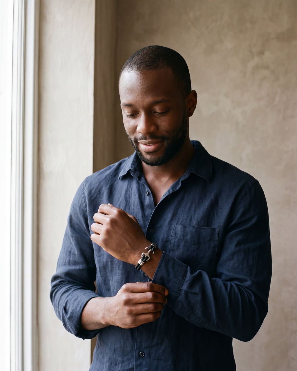 Man in a navy linen shirt adjusting his cuff, wearing the silver Atlas braided leather anchor bracelet