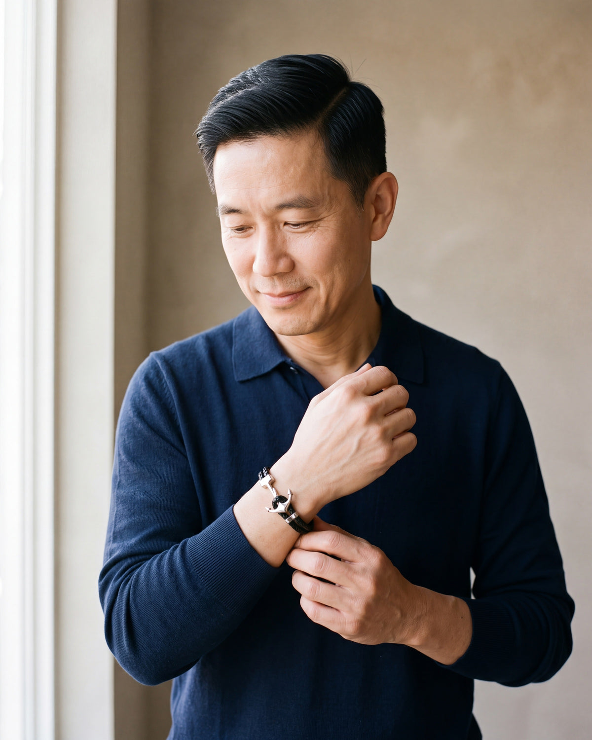 Man in a navy knit polo wearing the Atlas anchor hook bracelet in braided leather in black steel