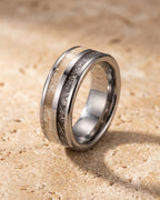 The Atlas antler and meteorite-pattern inlay tungsten ring standing on warm stone