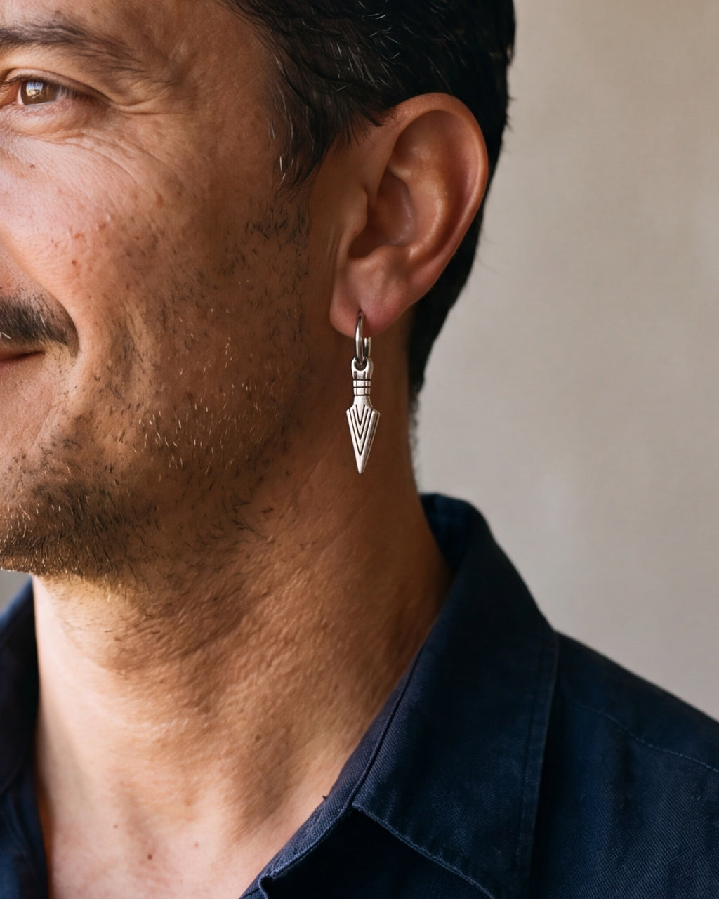Close-up of the Atlas arrowhead dangle hoop earrings in silver-tone steel, worn at true size