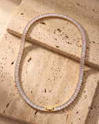 The gold-tone Atlas Baguette Tennis Chain laid on warm travertine stone